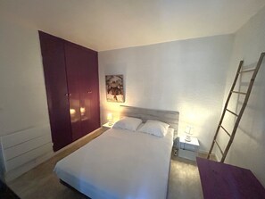 Ein Schlafzimmer mit einem Bett, einem Kleiderschrank, einem Nachttisch, einer Lampe, einem Bild an der Wand und einer Leiter.