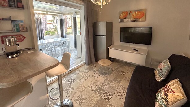Un espace de vie comprenant un canapé, un téléviseur, une machine à café, une table à manger avec des chaises et un sol à motifs.