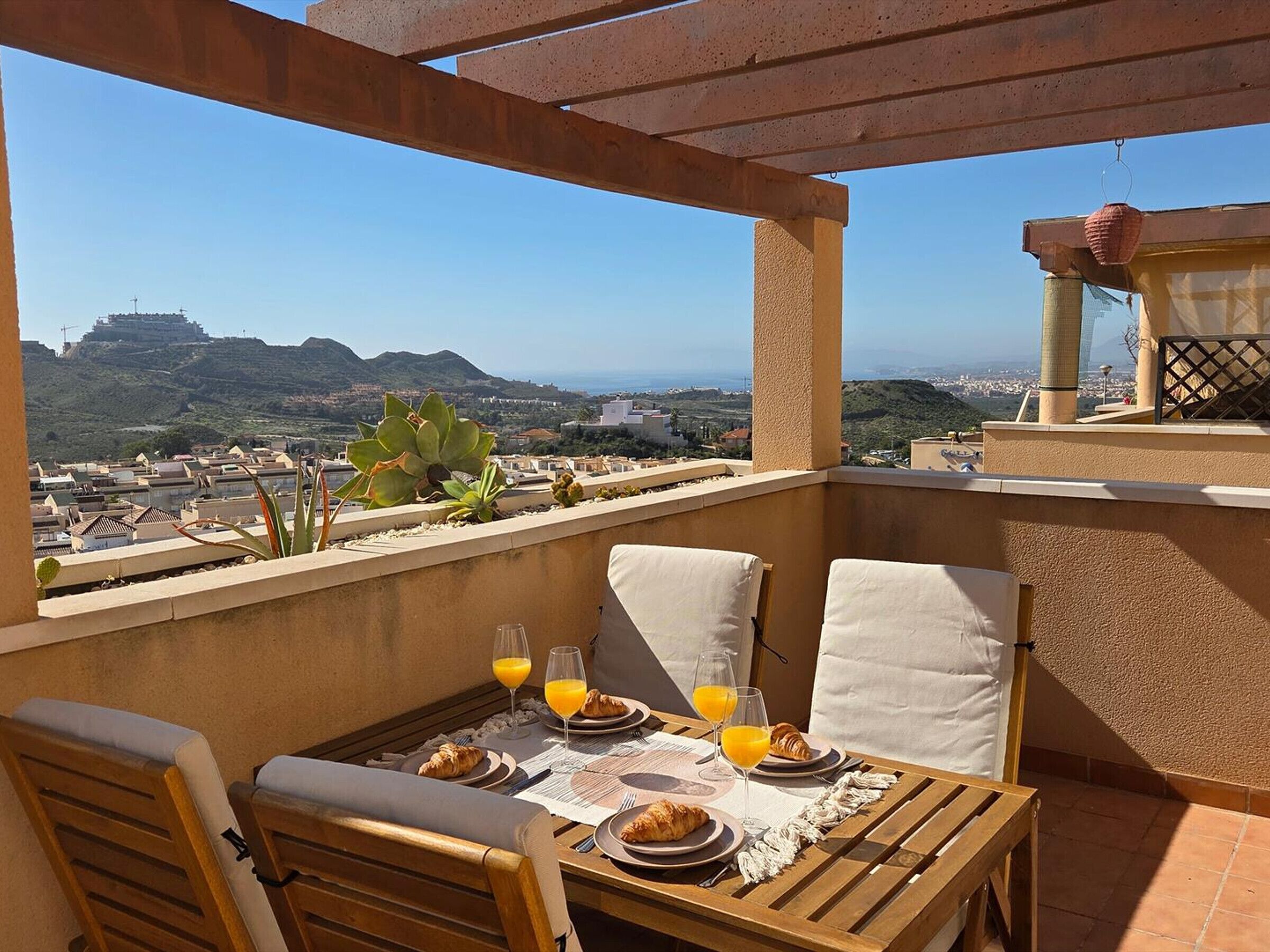 A balcony with a table set for breakfast, overlooking a cityscape and hills.