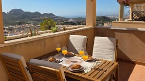Ein Balkon mit Frühstückstisch, mit Blick auf eine Stadtlandschaft und Hügel.