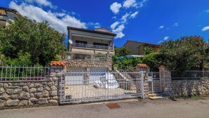 Una casa de dos pisos con fachada de piedra, un balcón y un camino de entrada con portón.