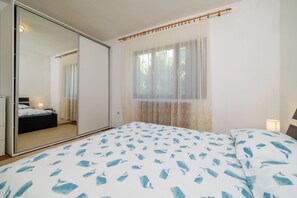 Ein Schlafzimmer mit Bett, Spiegel, Fenster mit leichtem Vorhang und Nachttischlampe.