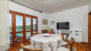 Un comedor con una mesa redonda, sillas, un televisor y vistas amplias por grandes ventanales.