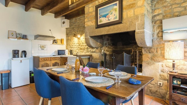 Zona pranzo con parete in pietra, camino e cucina sullo sfondo.