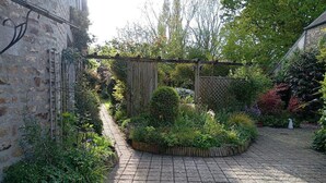 Un cortile pavimentato con una pergola in legno, un muro in pietra e diverse piante.