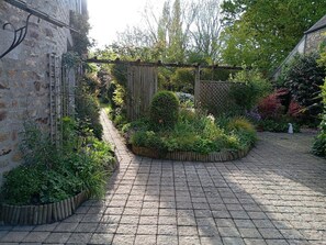Ein gepflasterter Innenhof mit einer Holz-Pergola, einer Steinmauer und verschiedenen Pflanzen.