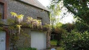 Un edificio in pietra con un portone garage bianco, un giardino con arbusti verdi e due poltrone Adirondack blu.