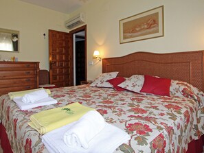 Ein Hotelzimmer mit Bett, einem Holzkasten, einem Nachttisch, einer Wandlampe und einer Tür.
