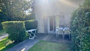 Un patio con mesa y sillas, una puerta corrediza de vidrio y un seto.