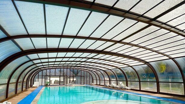 Una piscina techada con techo curvo y paneles de vidrio transparente.