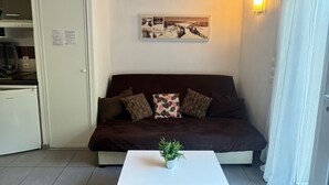 Un espacio habitable compacto con sofá, una mesita de centro, un cuadro colgado en la pared y una zona de cocina.