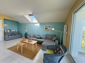 Ein Wohnzimmer mit einer Couch, einem Couchtisch, einem Korbstuhl, einer Stehlampe und einem Oberlicht.