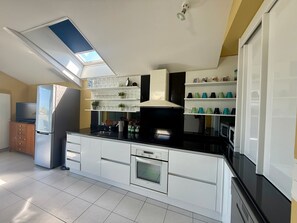 Eine moderne Küche mit Dachfenster, weißen Schränken, einer schwarzen Arbeitsplatte und einem eingebauten Backofen.