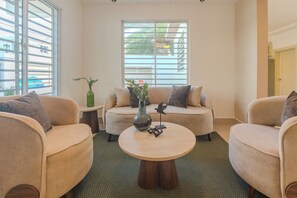 Uma sala de estar com sofá, duas poltronas, uma mesa de centro e uma janela com persianas.
