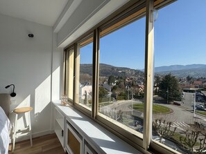 Ein Zimmer mit großem Fenster, Heizkörper, kleinem Hocker und Lampe.
