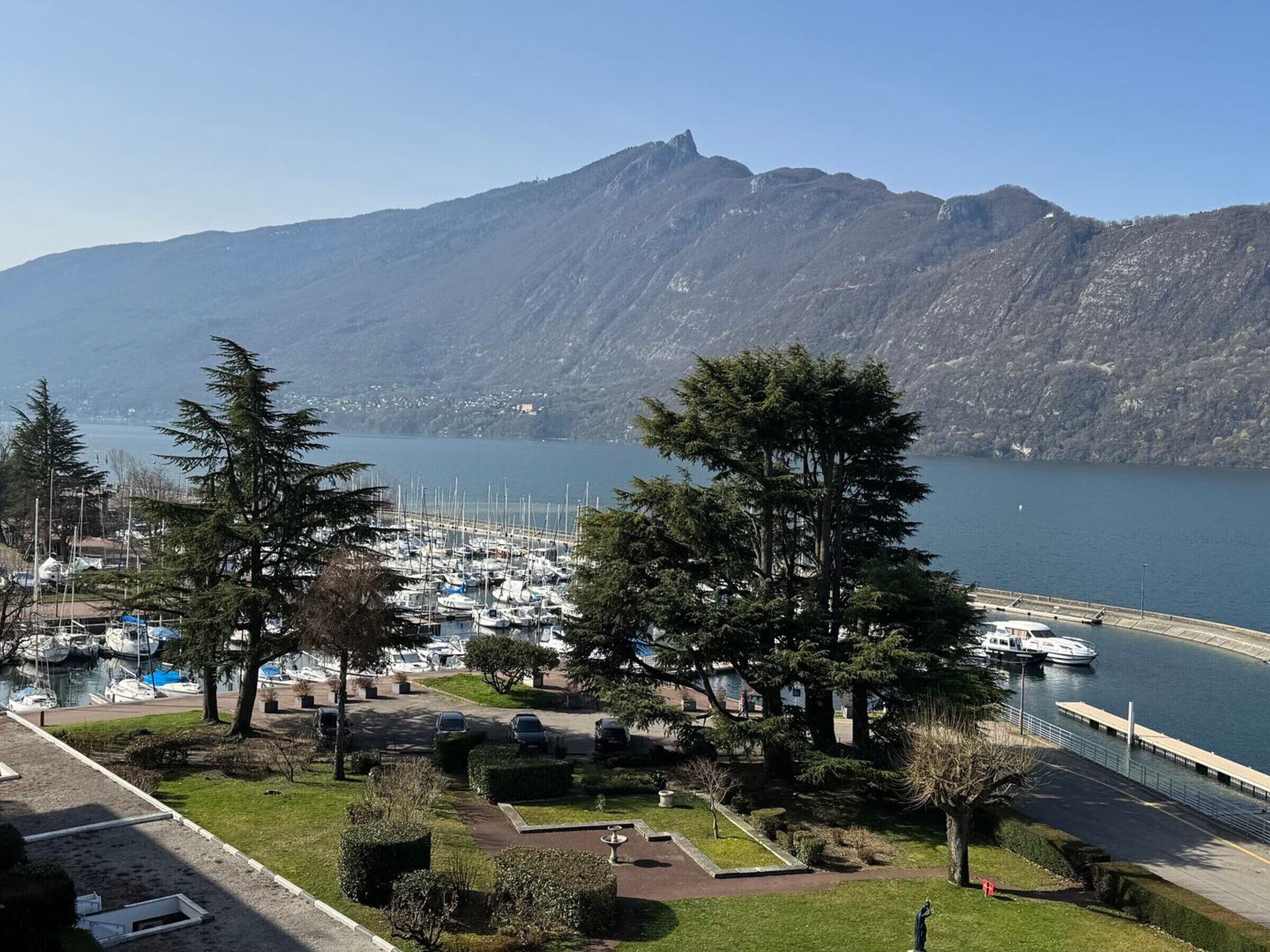 Un puerto deportivo con barcos amarrados, rodeado de árboles y una montaña al fondo.