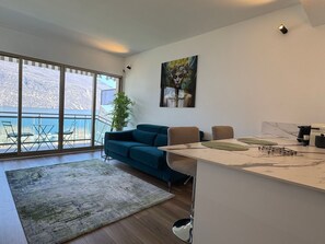 A modern living room with a large window, a blue sofa, a dining table with chairs, and a painting on the wall. - Renovated apartment, lake view, private parking (Aix-les-Bains)