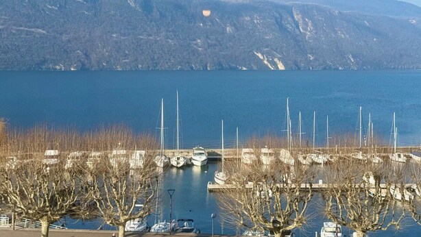 A marina with boats docked, a clear sky, and mountains in the background.
