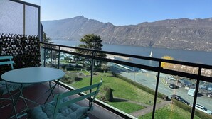 A balcony with a table and chairs, a view of a lake, and distant mountains.