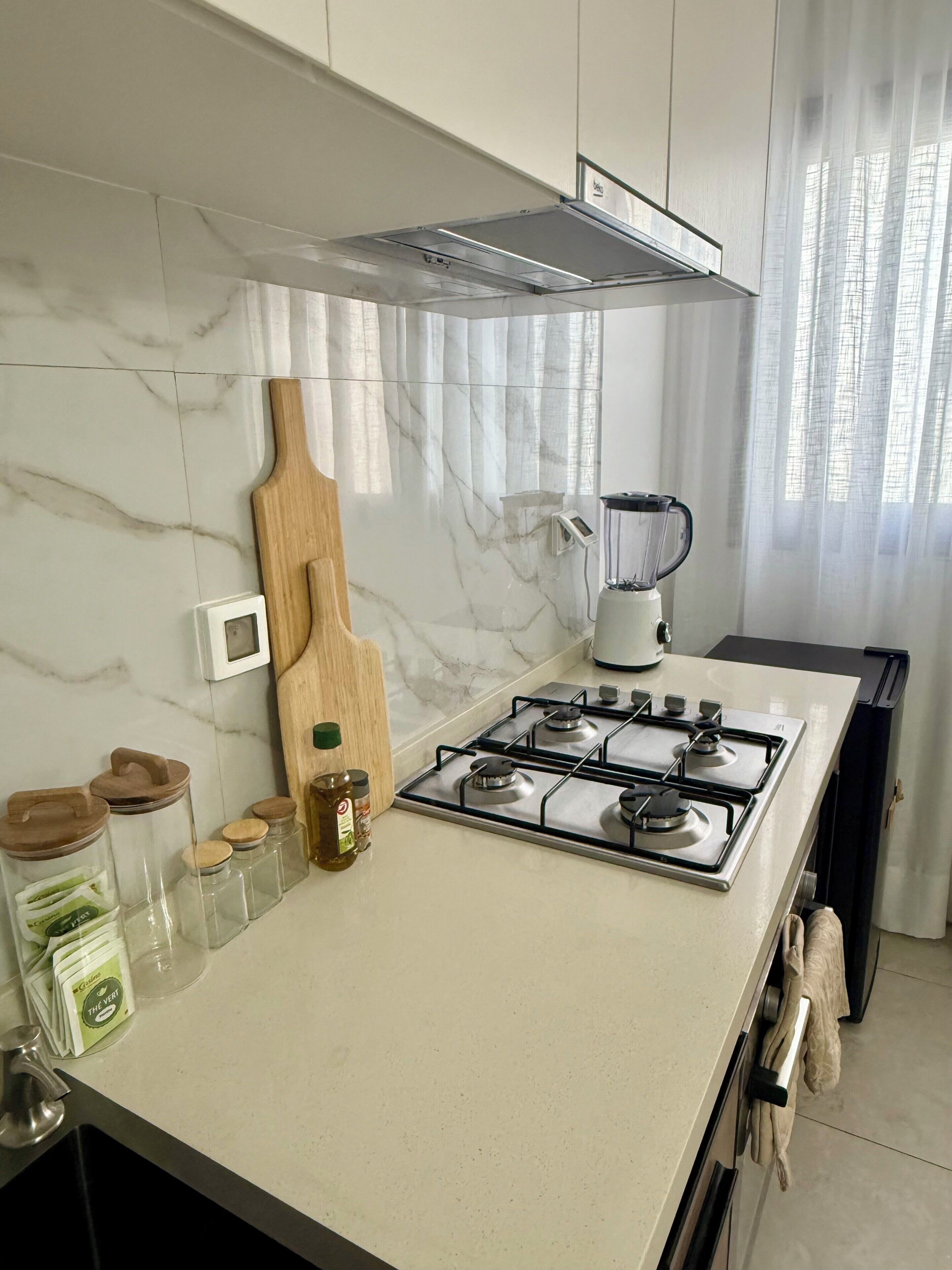 Una cucina moderna con piano cottura a gas, frullatore e diversi vasetti sul bancone.