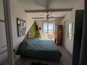 Ein Schlafzimmer mit einem Bett, einem Deckenventilator, einem Fenster mit Aussicht und Kunstwerken an den Wänden.
