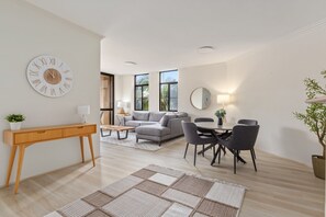 A modern living room with a sofa, dining table, chairs, a console table, and a large wall clock. - Bright 2-bed Retreat Near Darling Harbour (Sydney)