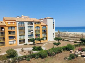 Ein mehrstöckiges Hotel mit Balkonen, Meerblick und einem angelegten Garten.