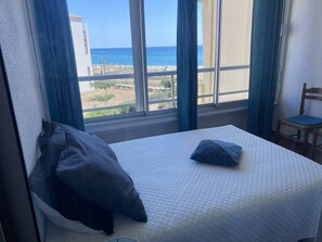 Ein Schlafzimmer mit Bett, Stuhl und Blick auf Strand und Meer.