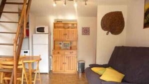 Un salon avec un canapé, une table à manger en bois et un coin cuisine équipé de placards et d’un four à micro-ondes.