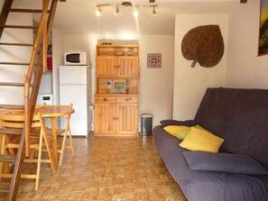 Ein Wohnzimmer mit einer Couch, einem Holzesstisch und einer Küchenzeile mit Schränken und einer Mikrowelle.