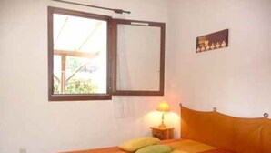 Une pièce avec un lit, une fenêtre, un tableau accroché au mur et une lampe de chevet.