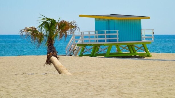 Une tour de surveillance avec une rambarde blanche et un toit bleu, située sur une plage de sable.