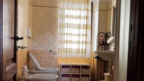 A bathroom with a toilet, bidet, vanity, and a window with a curtain.