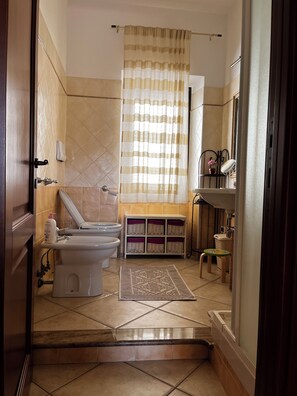 Een badkamer met toilet, bidet, wastafel en een raam met gordijn.