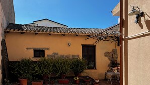 A courtyard with potted plants, a stone floor, a small window, and a wall-mounted light fixture.