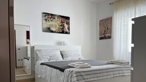 A modern bedroom with a bed, a painting, and a window with curtains.