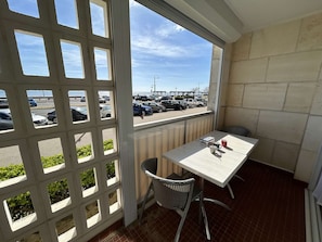 Un balcón con mesa y silla, vista a un estacionamiento y un edificio con suelo de baldosas.