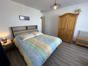 Une chambre à coucher comprenant un lit, une table de chevet, une armoire en bois, une chaise et un luminaire suspendu.
