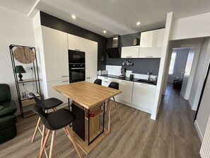 A modern kitchen with white cabinets, a wooden dining table, and a black stove. - Apartment sea view - 4/5 guests (Saint-Jean-de-Monts)