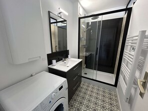 Une salle de bain moderne équipée d’un lave-linge, d’un évier, d’un miroir et d’une douche à parois en verre.