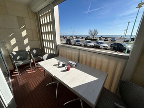 Un balcon avec une table, des chaises et une vue sur un parking et la plage.