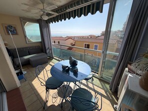 Ein Balkon mit Tisch und Stühlen, einer Couch und Blick auf Gebäude sowie das Meer.