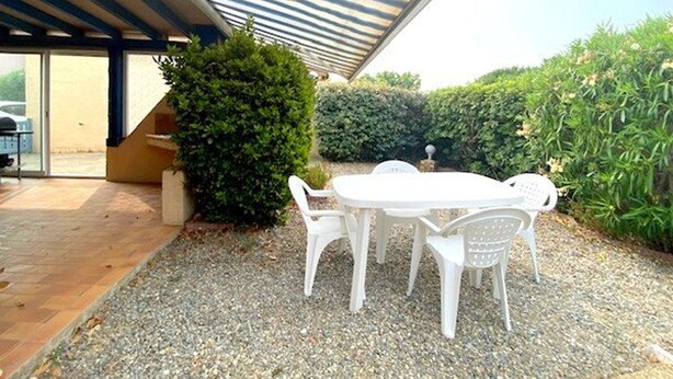 En udendørs patio med et bord og stole, et overdækket siddeområde og en grussti.