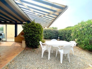 Une terrasse extérieure avec une table et des chaises, un espace salon abrité et un chemin de gravier.