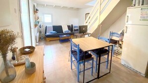 En kompakt opholdsstue med sofa, spisebord, computer og køleskab.