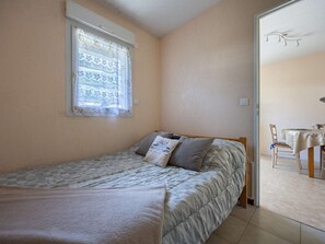 Ein Schlafzimmer mit Bett, einem Fenster mit Spitzenvorhängen, einer Tür zu einem Essbereich und einem Deckenventilator.