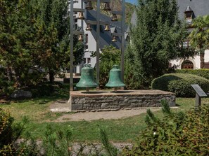 Ein Glockenturm mit zahlreichen Glocken, umgeben von Grün und einer Steinterrasse.