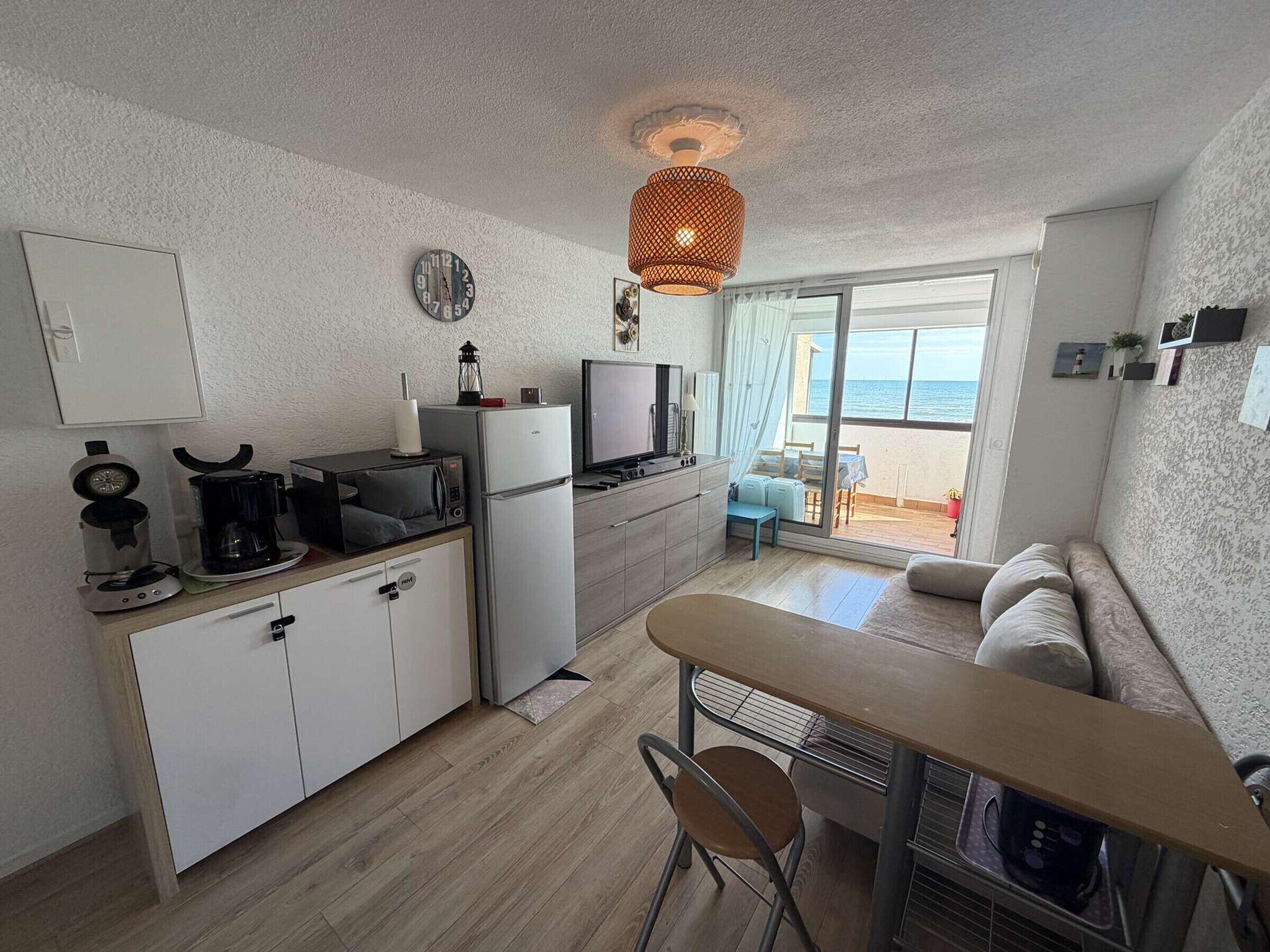 Een compacte keuken met een koelkast, magnetron, koffiezetapparaat en een klein eethoekje met een tafel en stoelen.