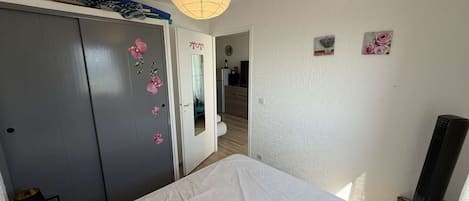 A bedroom with a bed, a wardrobe with floral stickers, a mirror, a ceiling light, and a small plant on the wall.