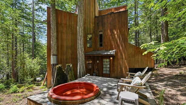 A wooden cabin with a hot tub, deck chairs, and a forest backdrop. - Moonraker House | Redwoods, Hot Tub & Trails (Sea Ranch)